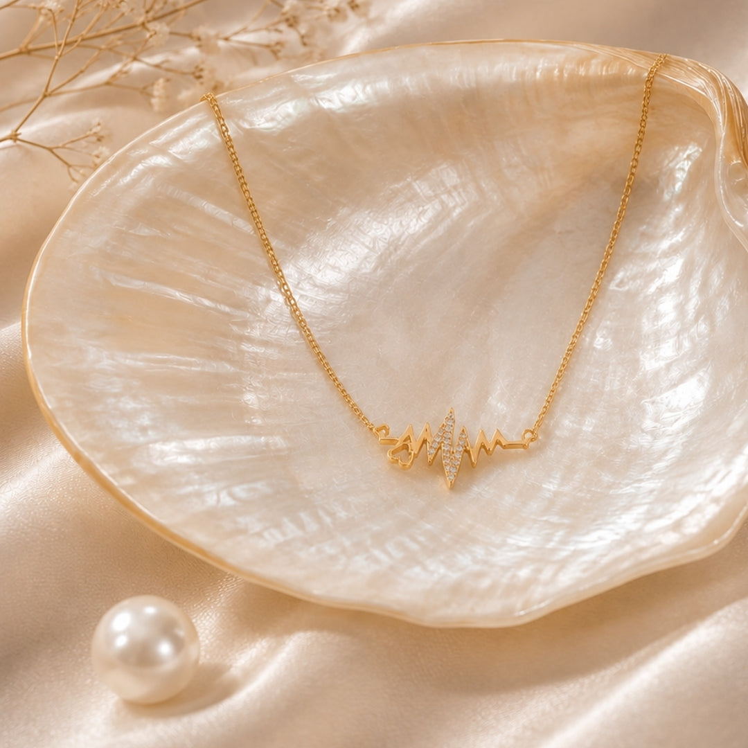 Gold-tone heartbeat-inspired pendant necklace styled on a shell dish